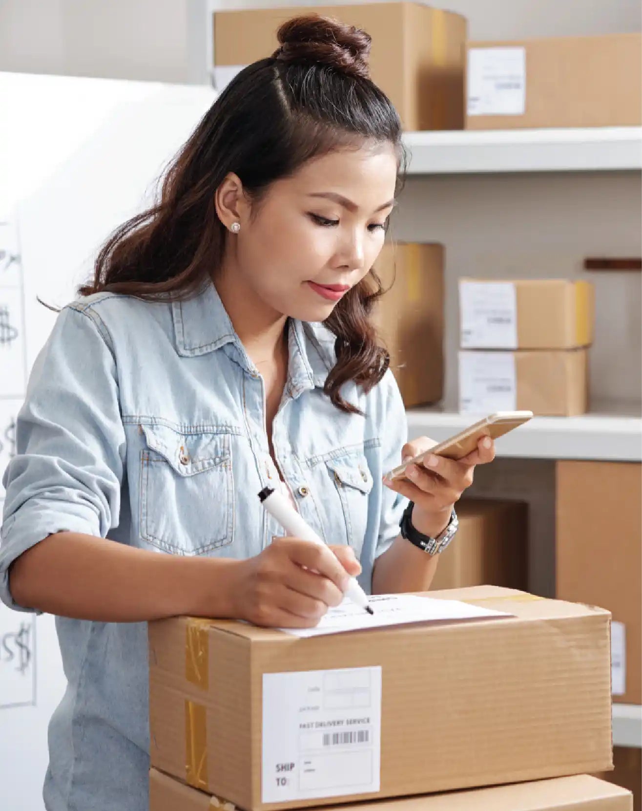 Warehouse staff preparing and labeling a packaged order while checking shipment details on a mobile device.