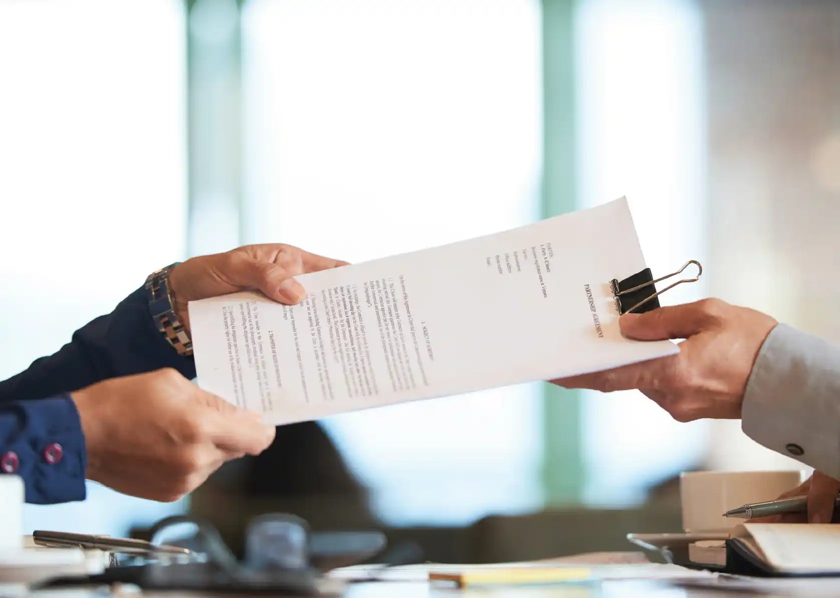 Hands exchanging completed application documents with a binder clip during the submission process.