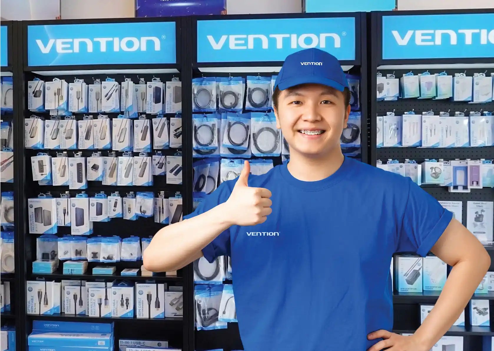 Vention store representative giving a thumbs up in front of a display wall of electronic accessories.