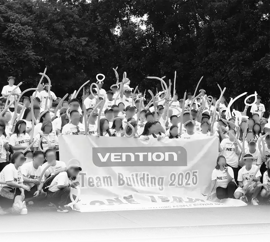 A large group of employees at the Vention Team Building 2025 event holding long balloons and a banner that says "ONE TEAM."