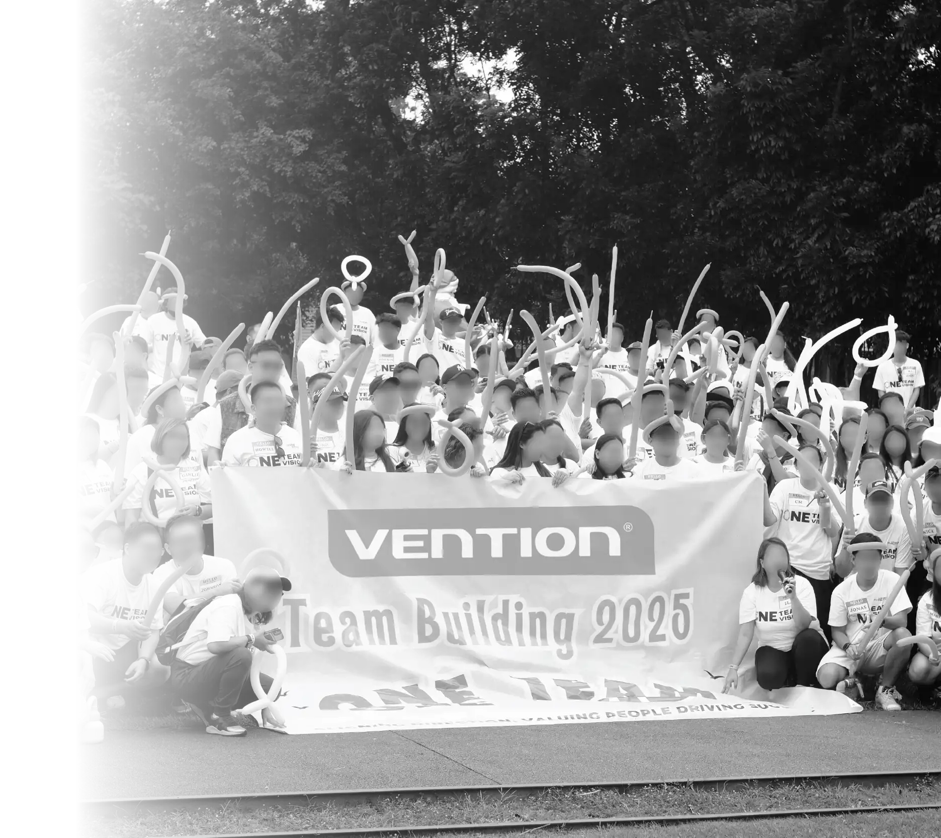 A large group of employees at the Vention Team Building 2025 event holding long balloons and a banner that says "ONE TEAM."