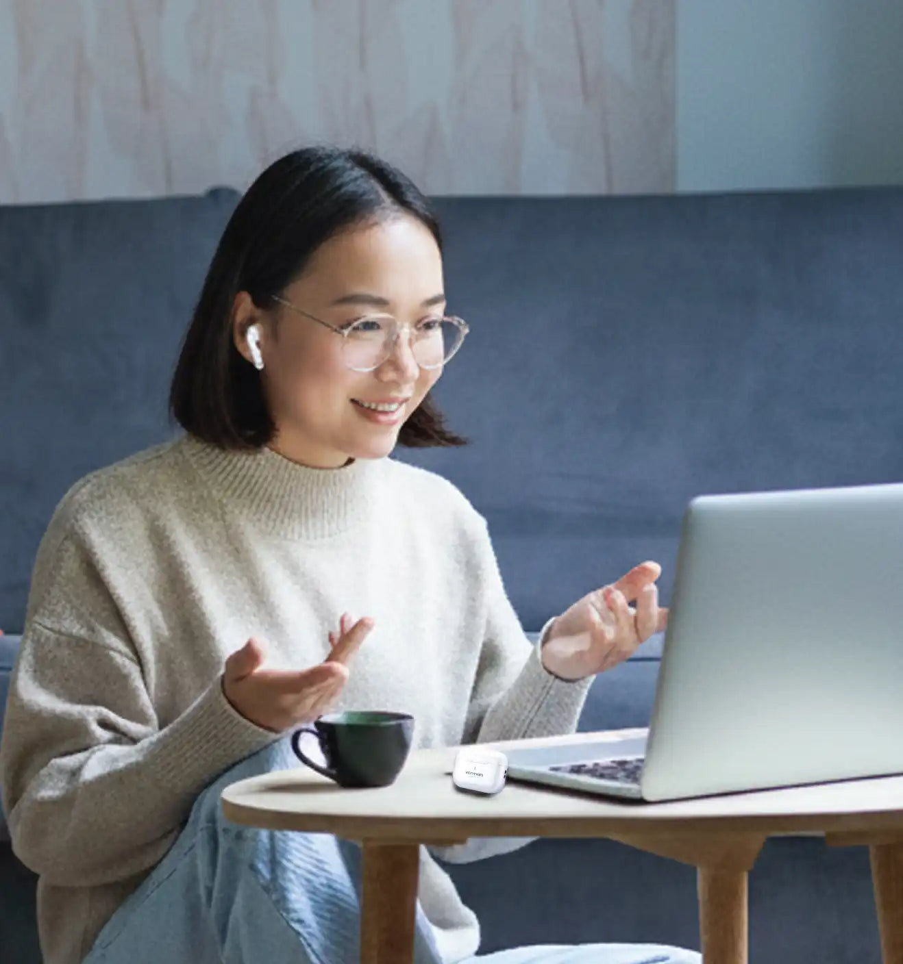 Woman sitting on a couch with a laptop and a cup, engaged in a video call.